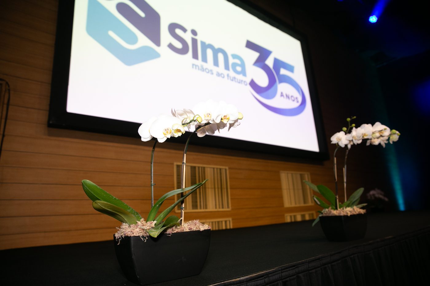 Telão com o logo Sima 35 anos e orquídeas no palco